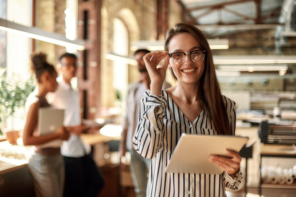 Successful business woman. Young cheerful woman holding digital tablet and looking at camera with