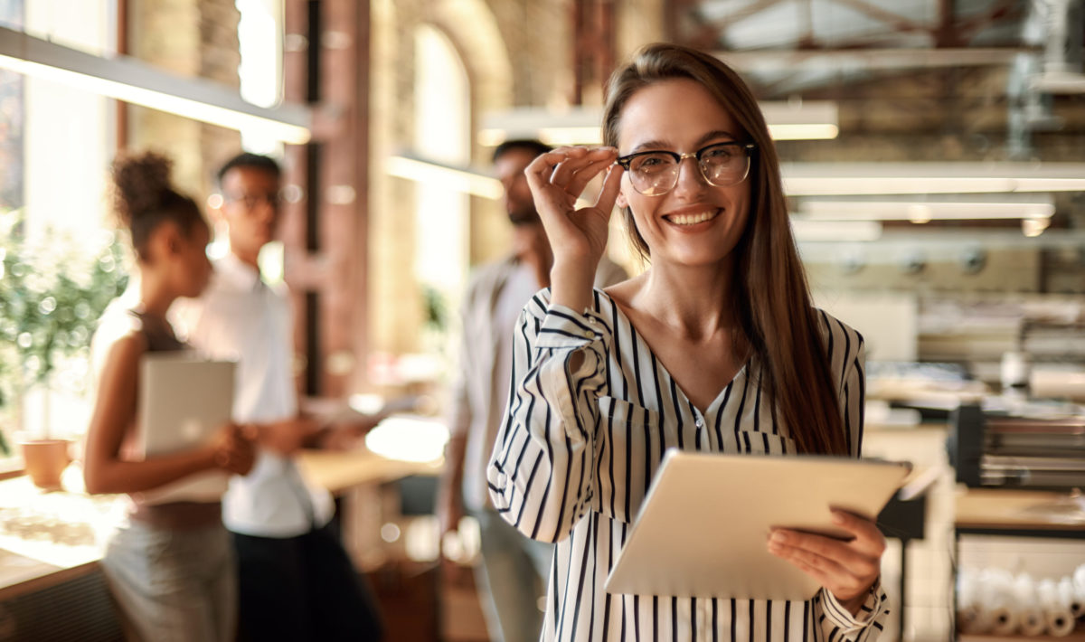 Successful business woman. Young cheerful woman holding digital tablet and looking at camera with